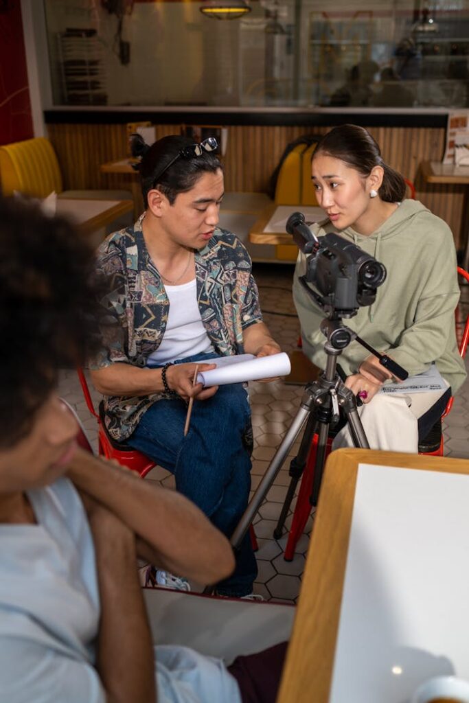 Two people collaborating on a film project in a cozy cafe setting, discussing camera work.